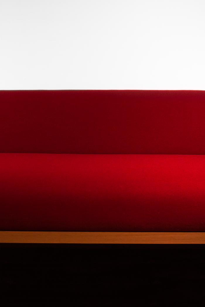 A modern red couch with wooden trim against a minimalist white wall, emphasizing clean lines and vibrant color contrast.